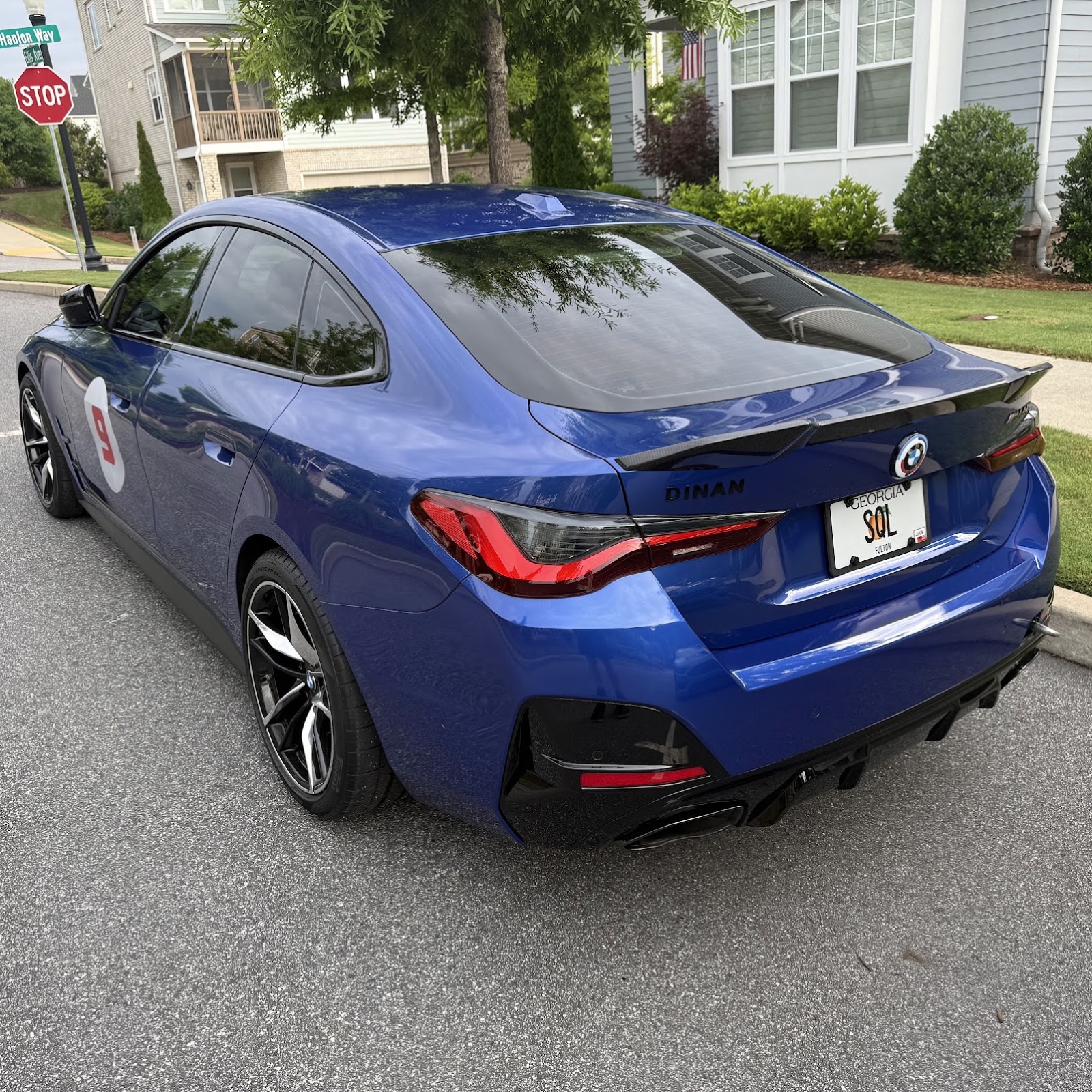 A blue BMW M440i from the rear three-quarter view, parked in a residential driveway. The DINAN badge is visible on the trunk lid; the license plate reads SQL.